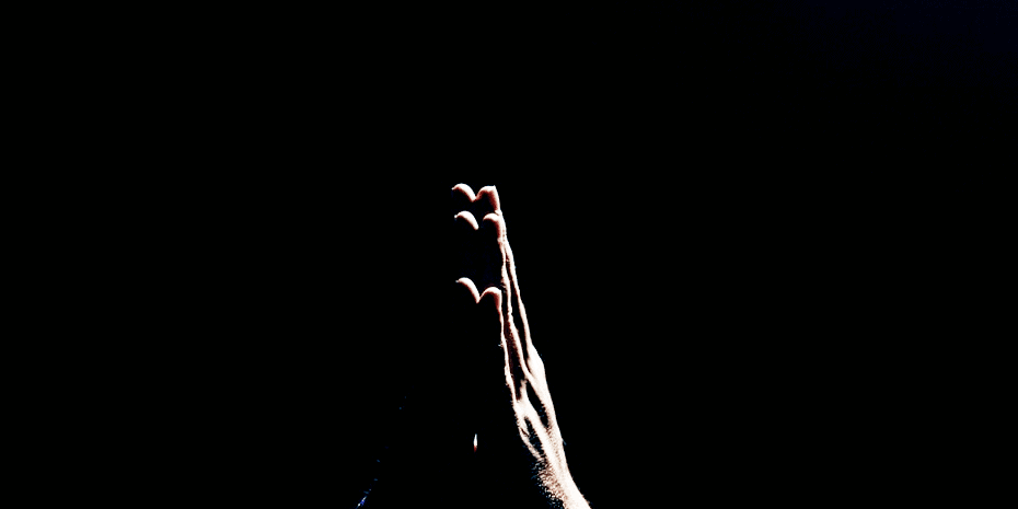 hands folded in prayer against black backdrop